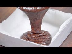 a chocolate cake in a white box on a wooden table, being drizzled with chocolate icing