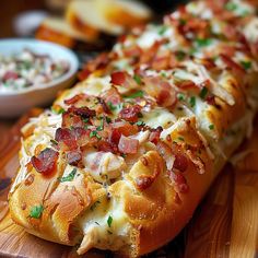 a long piece of bread with bacon and cheese on it next to a bowl of salad