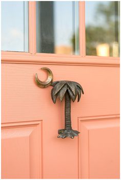 a door handle with a palm tree and crescent hanging from it's side on a pink door