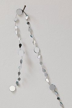 a long necklace with circles hanging from it's side on a white wall next to a vase