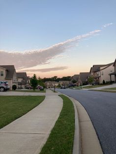 an empty street with houses and cars parked on the other side at sunset or dawn