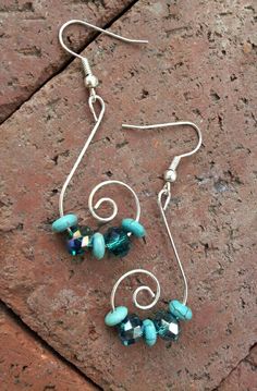 two pairs of earrings with blue beads and silver hooks on a brick surface in front of a stone wall