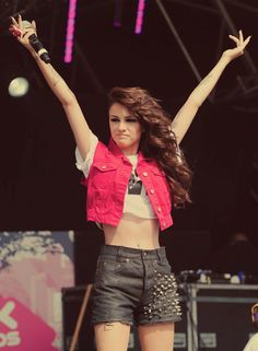 a woman with her arms up in the air on top of a stage, wearing black pants and a pink crop top