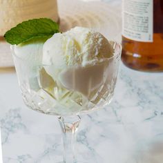 two scoops of ice cream sit in a glass on a marble table next to a bottle