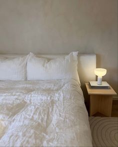 a bed with white linens and pillows in a small room next to a night stand