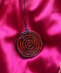 a red and black necklace is on a pink satin material with an intricate spiral design