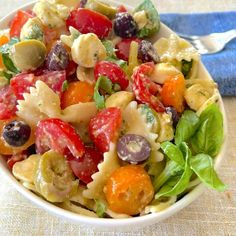 a white bowl filled with pasta salad on top of a blue cloth next to a fork