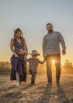 a man, woman and child are walking through the field at sunset in this family photo