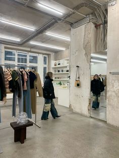 a woman walking through a clothing store next to clothes on racks and mannequins