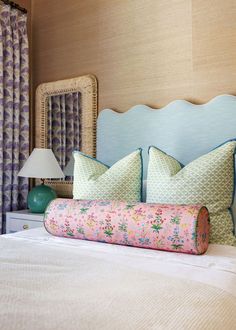 a bed with two pillows on top of it next to a mirror and lamp in a room