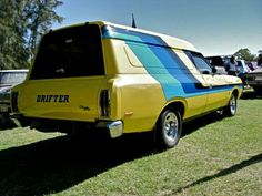 a yellow and blue van parked on top of a grass covered field next to other cars