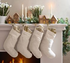 three stockings hanging from a mantel with candles and flowers in front of the fireplace