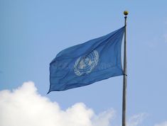 the united nations flag flies high in the blue sky with clouds behind it stock photo