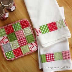 two pieces of quilt sitting on top of a wooden table next to some jars and napkins