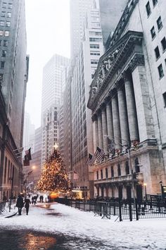 a christmas tree is in the middle of a snowy street with tall buildings behind it