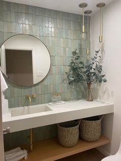 a bathroom sink with two baskets under it and a round mirror above the sink, next to a toilet