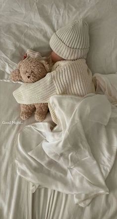 a teddy bear laying on top of a white blanket next to a hat and sweater