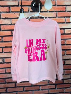 Calling all princesses! If you are in your official princess era, this long sleeve tee is a must have!  Text is in the trendy wavy style, with some white and gold glitter accents (don't worry - glitter will NOT come off!)  And a gold shimmer is all over the front and back of the shirt for that extra sparkle that every princess needs!  This makes a special birthday gift!!  Shirts are unisex fit and pre-shrunk.  https://hilhandmadeit.etsy.com Please Read Before Purchase!  If you are looking for so Pink Birthday Top With Text Print, Pink Birthday Tops With Text Print, Pink Tops With Text Print For Birthday, Pink Long Sleeve Top For Birthday, Pink Long Sleeve T-shirt With Name Print, Pink Glitter Print Top For Birthday, Princess Era, Princess Shirt, Wavy Style