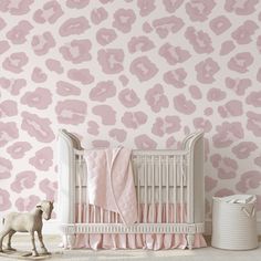 a baby crib in front of a pink wallpapered with leopard prints and a toy horse