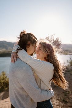 two women embracing each other in front of a lake