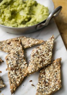 some crackers are on a plate next to a bowl of guacamole