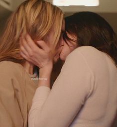 two women are kissing each other in front of a tv screen and the woman is wearing a sweater