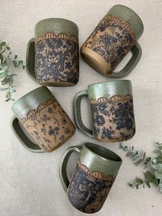 four coffee mugs sitting on top of a table next to some flowers and leaves