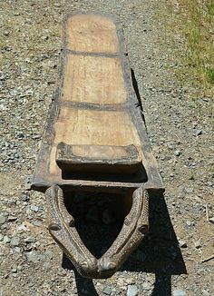 an old wooden sled sitting on top of a gravel road next to a field