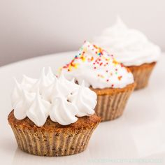 three cupcakes with white frosting and sprinkles are on a plate