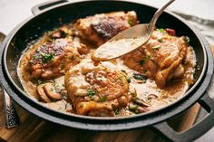 a pan filled with chicken and mushrooms on top of a wooden cutting board next to a fork