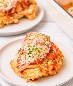 two white plates topped with lasagna covered in melted cheese and parmesan