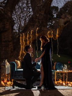 a man kneeling down next to a woman in front of a table with candles on it