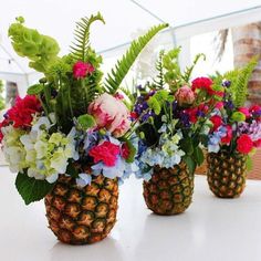 three pineapple vases filled with colorful flowers and greenery on a white table