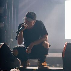 a man sitting on top of a stage while holding a microphone to his mouth,