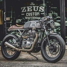 a motorcycle parked in front of a store with other motorcycles behind it and the words zeius custom written on the window