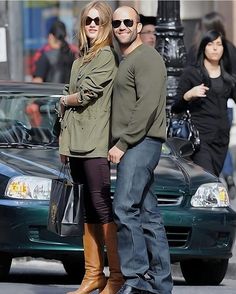 a man and woman standing next to each other in front of a car on the street