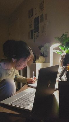 a woman sitting in front of a laptop computer on top of a wooden desk next to a plant