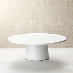 a white cake plate sitting on top of a table next to a beige wall and floor