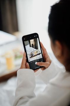 a woman is holding up her cell phone to take a selfie with the bed in the background