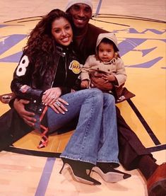 a man and woman sitting on top of a basketball court with a baby in their lap