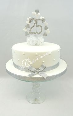 a white cake with silver decorations and a number 25 on top is sitting on a clear pedestal