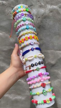 a hand holding a stack of bracelets on top of a white tube filled with lots of different colored beads