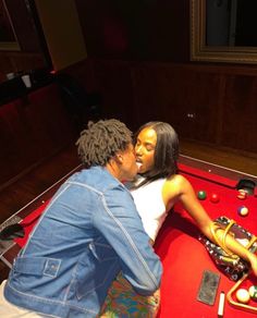 a man and woman sitting on top of a red pool table next to each other