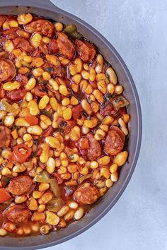 a skillet filled with beans and sausages on top of a white countertop