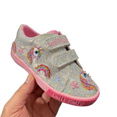 a hand holding up a shoe with sequins on the side and pink outs