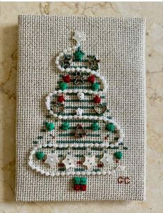 a christmas tree made out of beads on a piece of white fabric with green and red decorations