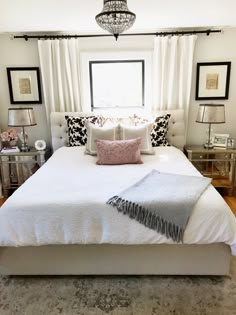 a white bed sitting in a bedroom next to a window with curtains and pillows on top of it