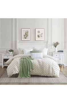 a white bed with green and white polka dot bedspread, pillows and blankets