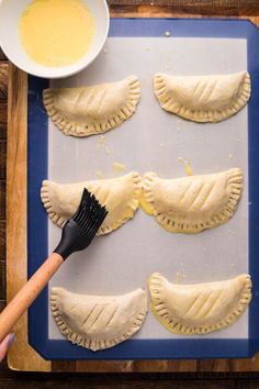 four pastries on a baking sheet with a spatula and bowl of sauce next to them