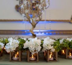 small vases filled with white flowers and lit candles on top of a table in front of a chandelier